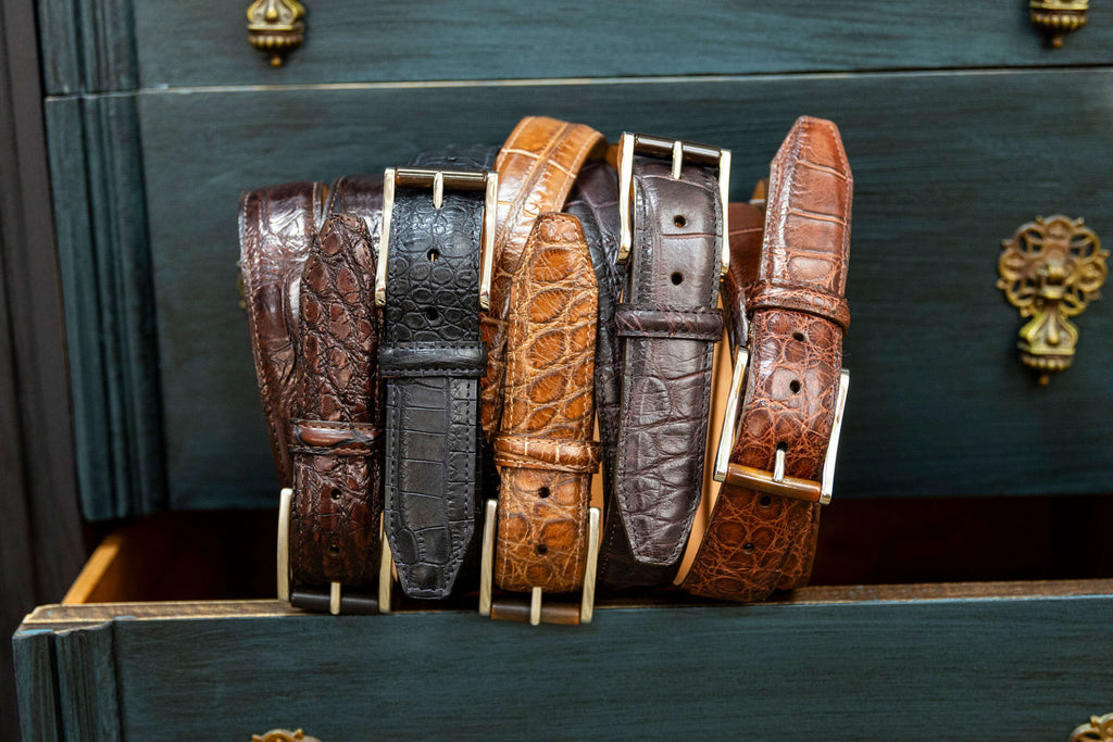 5 Genuine American Alligator Belts in the matte colors walnut, black, and chestnut, and in the vintage colors, old hickory and old walnut, rolled and propped on a vintage chest of drawers
