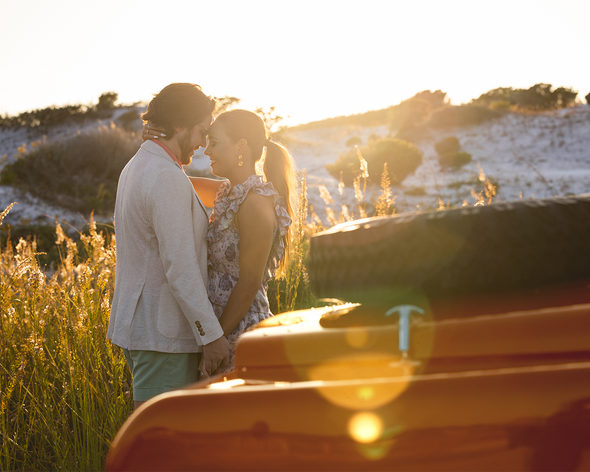Man and woman having an intimate moment at sunset by a red vehicle.