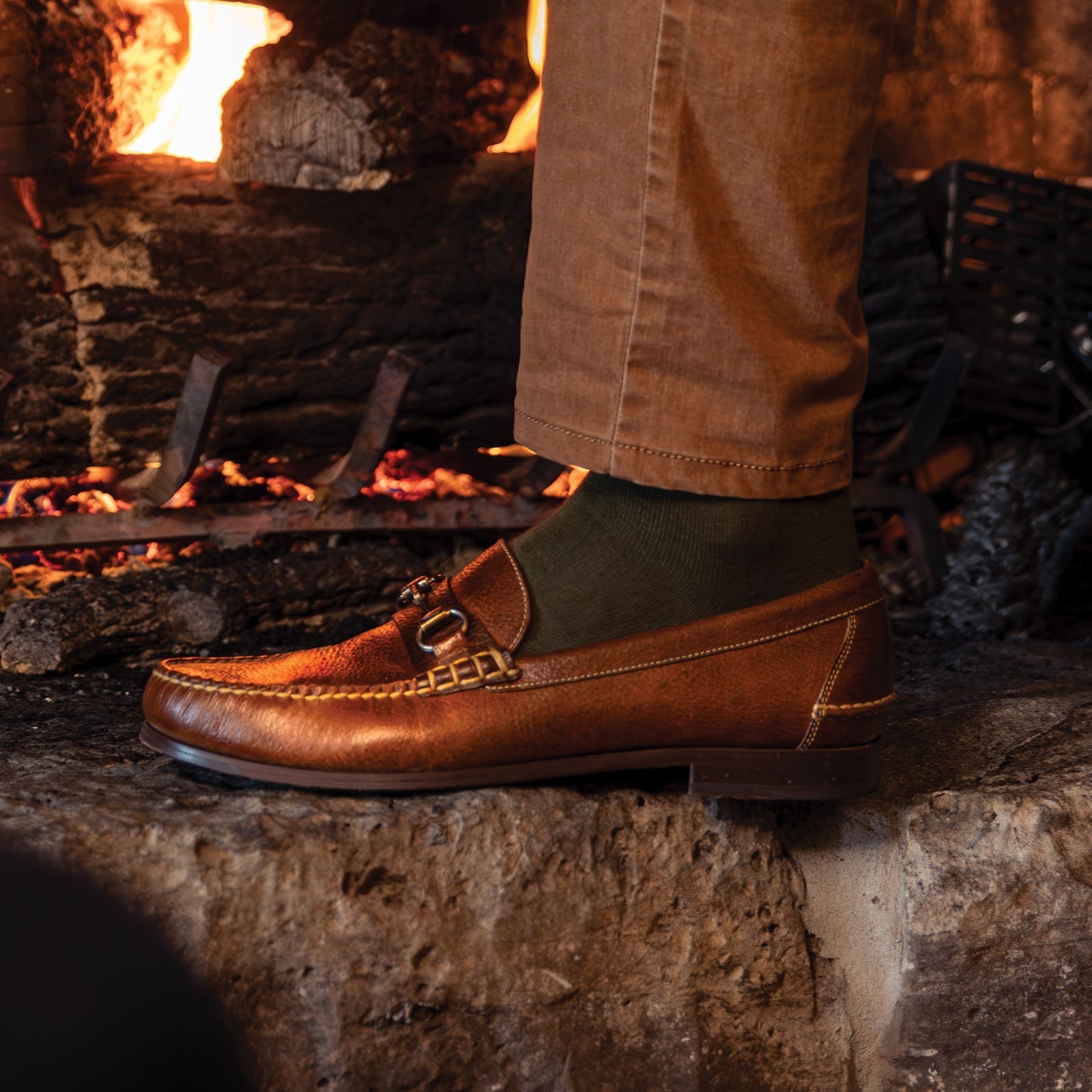 Brown leather shoes on a stone surface with a fireplace in the background