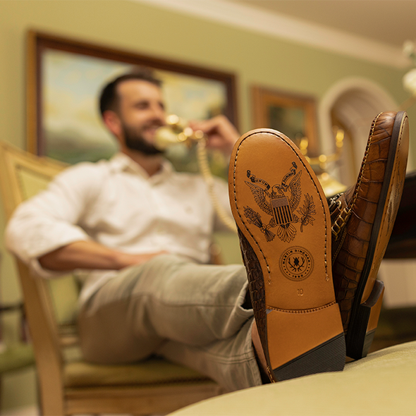 Person sitting with feet up on a table wearing brown dress shoes, blurred background of a room.