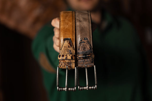 2 Franklin Italian Saddle Leather Belts being held for a side by side comparison of the silt and river rock colors.