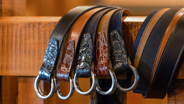 5 variants of Harrison O-Ring Leather Belts wrapped around a banister; walnut and whiskey calf leather belts, with navy, tobacco and walnut suede leather belts.